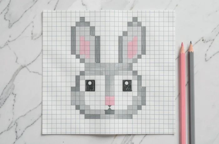 Pixel art d'un lapin vu de face sur papier quadrillé avec de grands yeux ronds et de longues oreilles en carrés gris et blancs